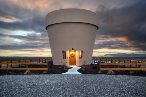 A unique round building with a door and a wreath, set against a dramatic sky and gravel pathway.